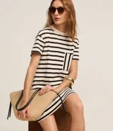 Vestido corto estilo camiseta de algodón, con cuello redondo, mangas cortas y bolsillo en el pecho. Presenta un patrón de rayas horizontales blancas y negras.