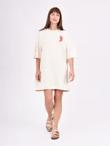 Remera de corte oversize color beige, con mangas cortas y cuello redondo. Presenta un pequeño estampado de un ají rojo en el lado izquierdo del pecho.