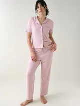 Camisa de manga corta para dormir de color rosado, confeccionada en viscosa. Presenta botones frontales, cuello con solapa, bolsillo en el pecho y ribetes a tono.