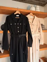 Mono de gabardina negro con cuello camisero, cierre frontal con botones metálicos, mangas largas y bolsillos tipo cargo en el pecho y las piernas. Incluye un cinturón ancho con hebilla del mismo tono para ajustar la cintura.