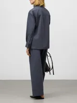 Camisa de algodón orgánico color gris oscuro, con cuello tipo tira, cierre frontal oculto con botones y manga larga. Presenta un diseño con cinturón fino integrado en la cintura para ajustar la silueta.