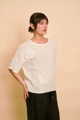 Blusa de lino color crudo con mangas cortas, cuello redondo y apliques florales bordados con detalles de pedrería y perlas en el frente.