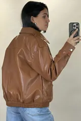 Chaqueta de ecocuero color marrón, de corte oversize, con cuello clásico, cierre frontal metálico, bolsillos laterales con solapa y puños con broches a presión.