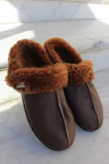 Pantufla de cuero color habano con interior de piel sintética, suela de goma y detalle de costura central.