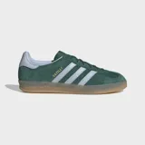 Championes Adidas Gazelle Indoor de gamuza verde oscuro, con las tres tiras características en color blanco y el nombre del modelo en letras doradas en el lateral. Poseen suela de goma translúcida y detalles en color celeste claro en el talón.