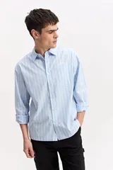 Camisa de manga larga de corte suelto, color celeste con diseño a rayas verticales, cuello clásico, bolsillo delantero en el pecho y cierre frontal con botones.