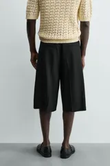 Bermuda negra de corte ancho (wide fit) con pliegues frontales, bolsillos laterales y bolsillos traseros de vivo.