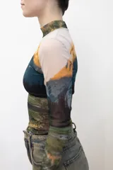 Remera crop top de mangas largas y cuello alto, confeccionada en tejido de red transparente con estampado de paisaje montañoso.