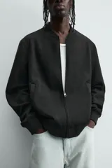 Cazadora bomber negra de corte regular fit, confeccionada en tejido efecto ante. Cuenta con cuello, puños y bajo en rib elástico, manga larga, bolsillos de vivo en la cadera y un bolsillo interior. Cierre frontal con cremallera.