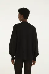 Buzo de punto negro, de corte holgado, con cuello redondo y mangas largas con puños ajustados. Presenta múltiples apliques bordados con motivos tropicales y coloridos en la parte frontal.