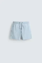 Bañador de hombre de largo medio, color celeste claro con rayas blancas horizontales. Presenta cintura elástica ajustable con cordón, bolsillos frontales y bolsillos traseros de plastrón. Incluye forro interior.