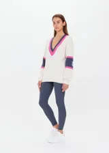 Sweater de punto color crema, con escote en pico con ribete rosa y gris. Presenta mangas largas con franjas grises y rosas en los puños, y logo bordado en el brazo.