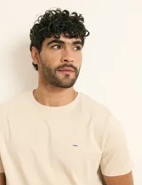 Remera básica de algodón color beige, de manga corta, con cuello redondo y un pequeño detalle bordado en el pecho.