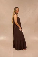 Vestido largo color marrón chocolate, con tirantes ajustables mediante lazos en los hombros, escote redondo fruncido y diseño amplio con volados en la parte inferior.