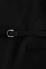 Blazer negro de corte recto con cuello elevado, hombreras y cierre frontal mediante cinturón fino ajustable. Presenta bolsillos delanteros ribeteados y aberturas en los puños.