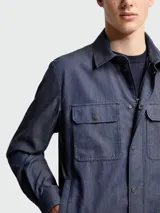 Camisa Moncler de jean azul oscuro, de manga larga, con cierre frontal de botones a presión, cuello clásico y dos bolsillos delanteros con solapa y botón.
