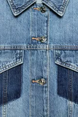 Cazadora corta de denim con cuello solapa y manga larga. Presenta un diseño de lavado combinado a contraste, con bolsillos de plastrón con solapa en el pecho y cierre frontal con botones metálicos.