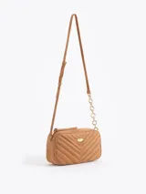 Bandolera de gamuza gris con diseño matelaseado en forma de V. Presenta un aplique metálico dorado en forma de labios en el frente y una correa combinada con cadena metálica dorada.