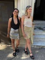 Falda corta de lentejuelas con diseño cruzado y detalle de lazo lateral. Presenta un acabado brillante con destellos iridiscentes.