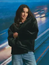 Campera de textura afelpada en color negro, con cuello redondo, cierre frontal con botones y bolsillos delanteros. Presenta detalles de terminaciones en material sintético liso a lo largo de la abertura y los bolsillos.