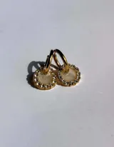 Aros de acero quirúrgico con dije circular de resina rosa y borde de strass dorados.