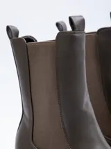 Bota tipo chelsea de caña alta confeccionada en cuero sintético, con paneles elásticos laterales, plataforma dentada y taco cuadrado.