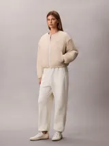Campera puffer Calvin Klein color beige, de cuello redondo, manga larga y cierre frontal con cremallera blanca. Presenta bolsillos laterales y un parche con logo bordado en el pecho.