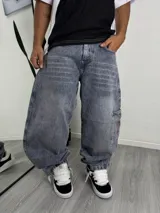 Pantalón de jean estilo baggy con lavado ácido en tono azul grisáceo, corte holgado y diseño de bolsillos tipo cargo con detalles bordados en rojo.