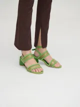 Sandalias de taco redondo de 6 cm, confeccionadas en gamuza verde con tiras frontales y de tobillo en material translúcido. Cuentan con cierre de pulsera al tobillo y plantilla de cuero.