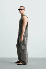 Camiseta sin mangas de punto acanalado, color verde oliva desgastado, con cuello redondo y abertura frontal en forma de 'V'. Presenta un estampado desvanecido en el centro del pecho.