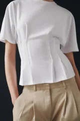 Camiseta de algodón con cuello redondo y manga corta. Presenta un diseño entallado con pinzas en la cintura y bajo recto.