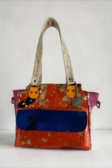 Cartera de cuero de diseño exclusivo con intervención artística de Carolina De Cunto, combinando tonos naranja, azul y detalles en color natu y terra. Cuenta con doble asa de hombro, solapa frontal de pelo sintético azul y herrajes metálicos.