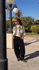 Chaleco negro con bordados blancos de estilo arabesco en el frente, sin mangas y con diseño abierto.