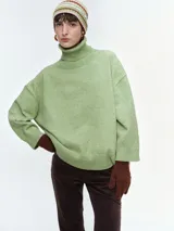 Buzo de tejido de punto color verde claro, con cuello alto acanalado, hombros caídos y mangas largas con puños acanalados.