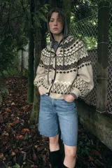 Chaqueta de punto con diseño jacquard de estilo nórdico, en tonos beige, marrón y blanco. Presenta capucha, cierre frontal con botones tipo trenca y mangas largas con puños ajustados.