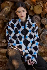 Campera de textura tipo corderito con diseño a cuadros en tonos marrones, negros y beige. Presenta cuello alto, cierre frontal completo y detalles en tela técnica lisa en los laterales y bordes. Posee un elástico ajustable en la parte inferior para regular el calce.