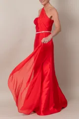 Vestido largo de fiesta color rojo, de corte recto y un hombro descubierto. Presenta una pieza de gasa que nace del hombro, formando el bretel y cayendo a lo largo del vestido.