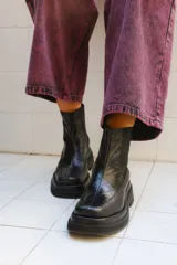 Bota de caña media color negro con textura de reptil en el empeine y paneles laterales elásticos. Presenta una suela de plataforma gruesa y punta cuadrada.