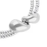Collar de dos vueltas compuesto por pequeñas cuentas metálicas bañadas en plata y un dije central con forma de dos gotas.