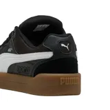 Championes Puma modelo Park Lifestyle SK8, de diseño urbano inspirado en el skate. Presentan una base de cuero blanco con detalles en gamuza gris claro en la puntera y el talón, destacando la icónica franja lateral de Puma en color negro. La suela es de goma color caramelo, proporcionando un contraste clásico y duradero.