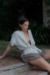 Saco de punto color beige con diseño de trenzas en los bordes frontales, manga corta y corte holgado. Presenta un estilo versátil ideal para diversas ocasiones.