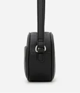 Cartera tipo camera bag pequeña, color marrón camel, de forma ovalada con superficie texturizada. Cuenta con correa ajustable larga, cierre principal con cremallera dorada y un pequeño bolsillo frontal con cremallera.