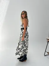 Vestido midi blanco con estampado floral negro, escote halter y cinturón ancho negro.