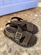 Sandalias negras de cuero con tiras cruzadas y ajuste con hebilla. Decoración de tachas plateadas en la suela.