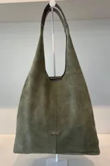 Bolso tipo tote de gran capacidad, confeccionado artesanalmente en cuero vacuno color marrón. Presenta un diseño minimalista con costura central vertical, fuelle lateral ajustable con cierre y placa metálica con logo en la parte inferior.