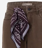 Pantalón de jean color marrón con corte baggy holgado, tiro medio y cierre frontal con cremallera y botón. Incluye un pañuelo estampado decorativo en la cintura.