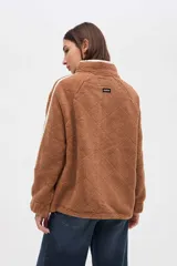 Campera de sherpa color marrón con diseño capitoneado, cierre frontal completo y detalles en color blanco. Presenta cuello alto, bolsillos laterales y puños elásticos.