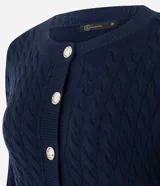 Cárdigan de punto trenzado color marrón, con cuello redondo, manga larga y cierre frontal con botones metálicos. Presenta puños y ruedo acanalados.