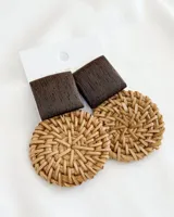 Aros colgantes con forma geométrica, con un cuadrado de madera marrón en la parte superior y un círculo de mimbre tejido en la parte inferior.