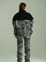 Campera de denim texturado con estampado abstracto en tonos grises y negros. Presenta un canesú superior en denim liso negro, cuello de piel sintética negra, cierre frontal con botones a presión color bronce y mangas largas.